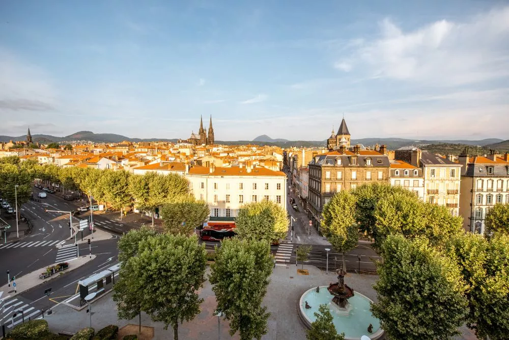 Vue aérienne de la ville de Clermont-Ferrand avec la cathédrale et les montagnes en arrière-plan.