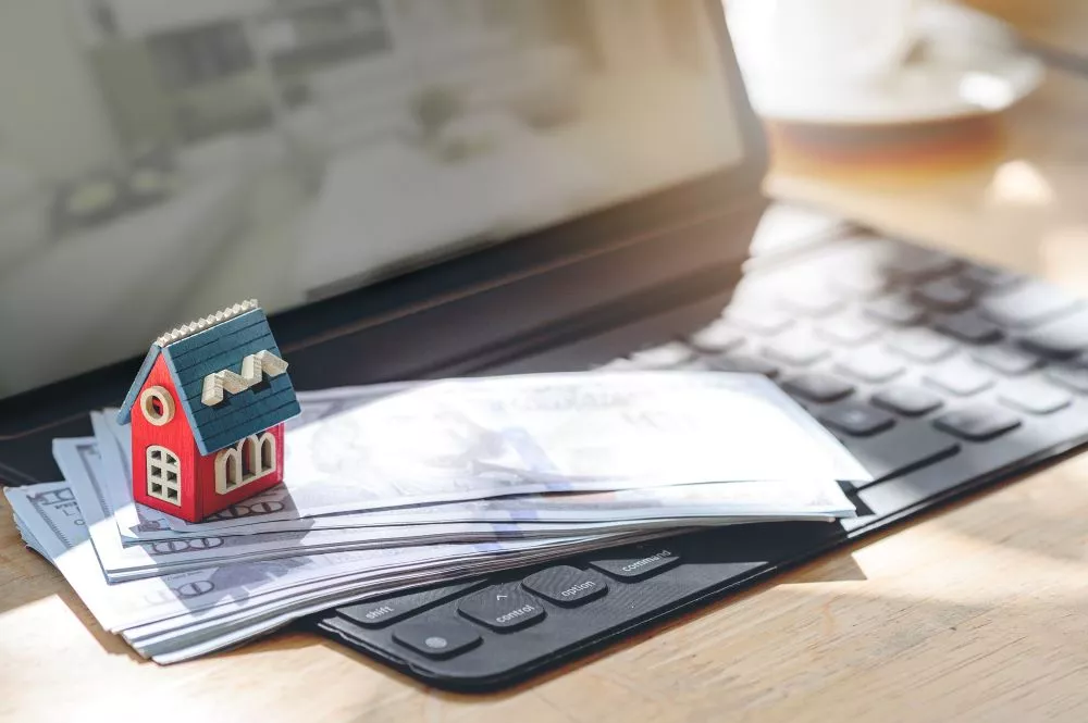 Une maison miniature posé sur des billets posés sur un clavier d'ordinateur