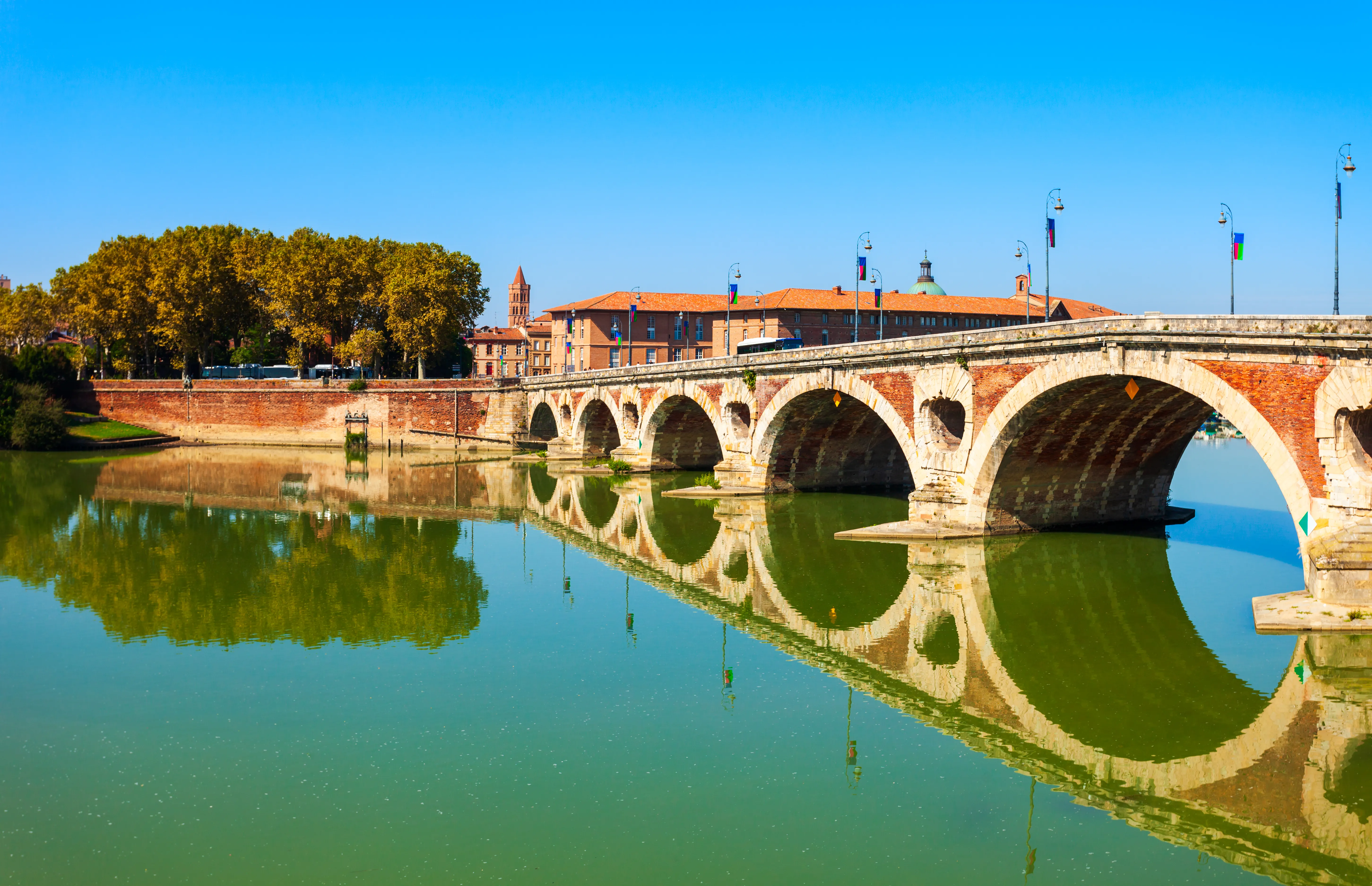 Pont Neuf de Toulouse en briques roses enjambant la Garonne, avec l’Hôtel-Dieu Saint-Jacques en arrière-plan