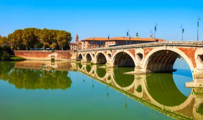 Pont Neuf de Toulouse en briques roses enjambant la Garonne, avec l’Hôtel-Dieu Saint-Jacques en arrière-plan